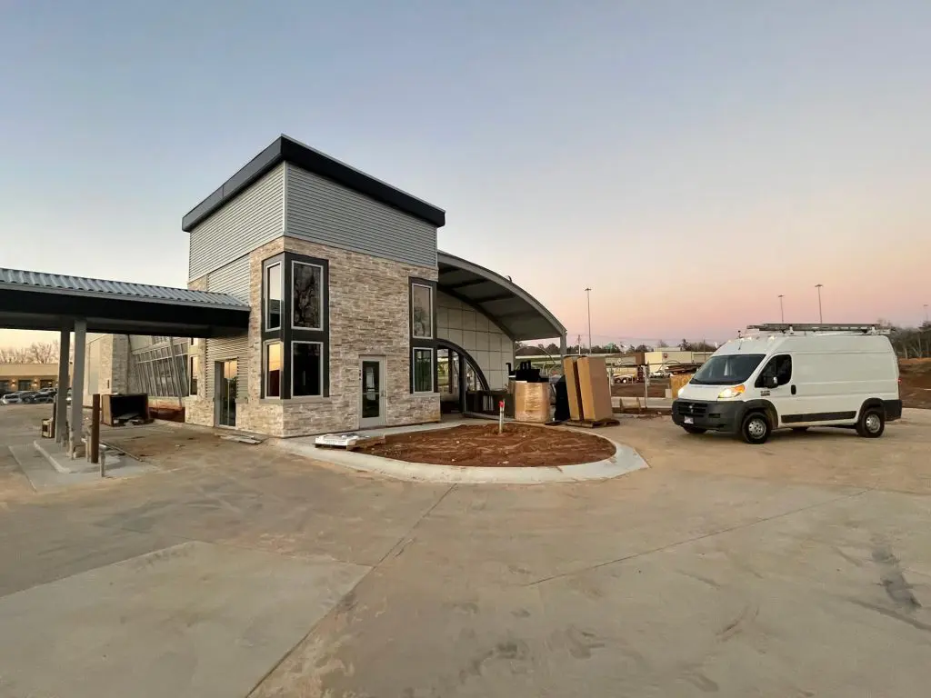 Commercial building exterior during repaint preparation by Local Painters in Tyler TX, featuring modern stonework, large windows, and contractor van on site.