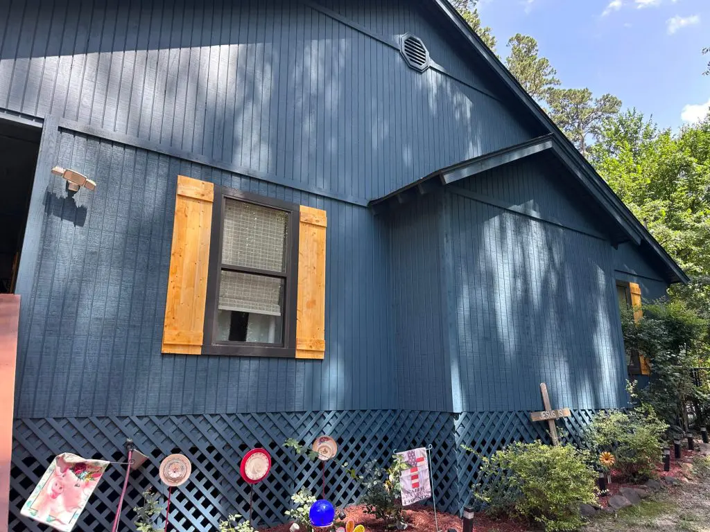 Expert exterior painting of board and batten siding in a custom dark blue color, accented by natural wood shutters on a lakeside residential home near Tyler, TX.