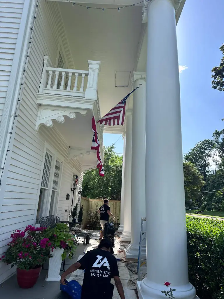 Z&A Custom Painting professional team performing thorough exterior surface preparation and cleaning on a large, classic white residential porch in the Tyler, TX area.