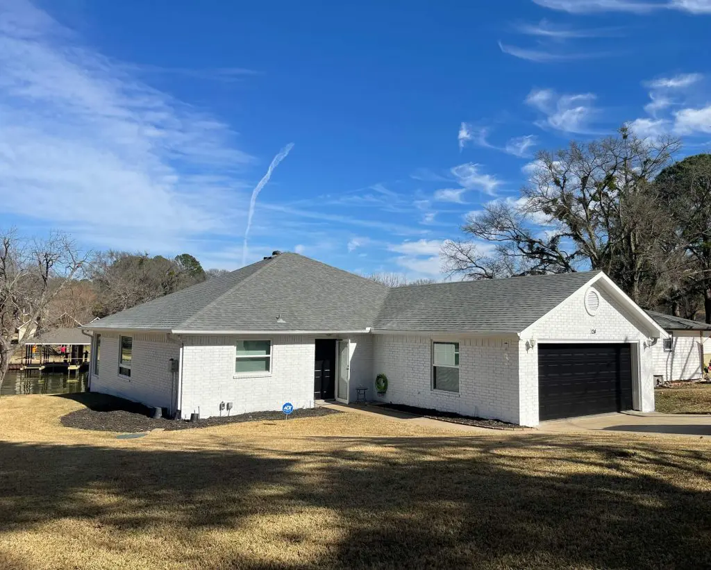 High-contrast exterior painting for a lakeside home, featuring bright white siding and a custom matte black garage door in the Tyler, TX area.