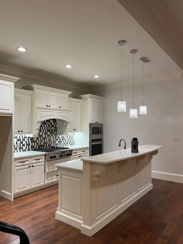 Expert cabinet painting and refinishing showcasing custom white kitchen cabinetry with detailed trim and a built-in breakfast bar in a Tyler, TX home.
