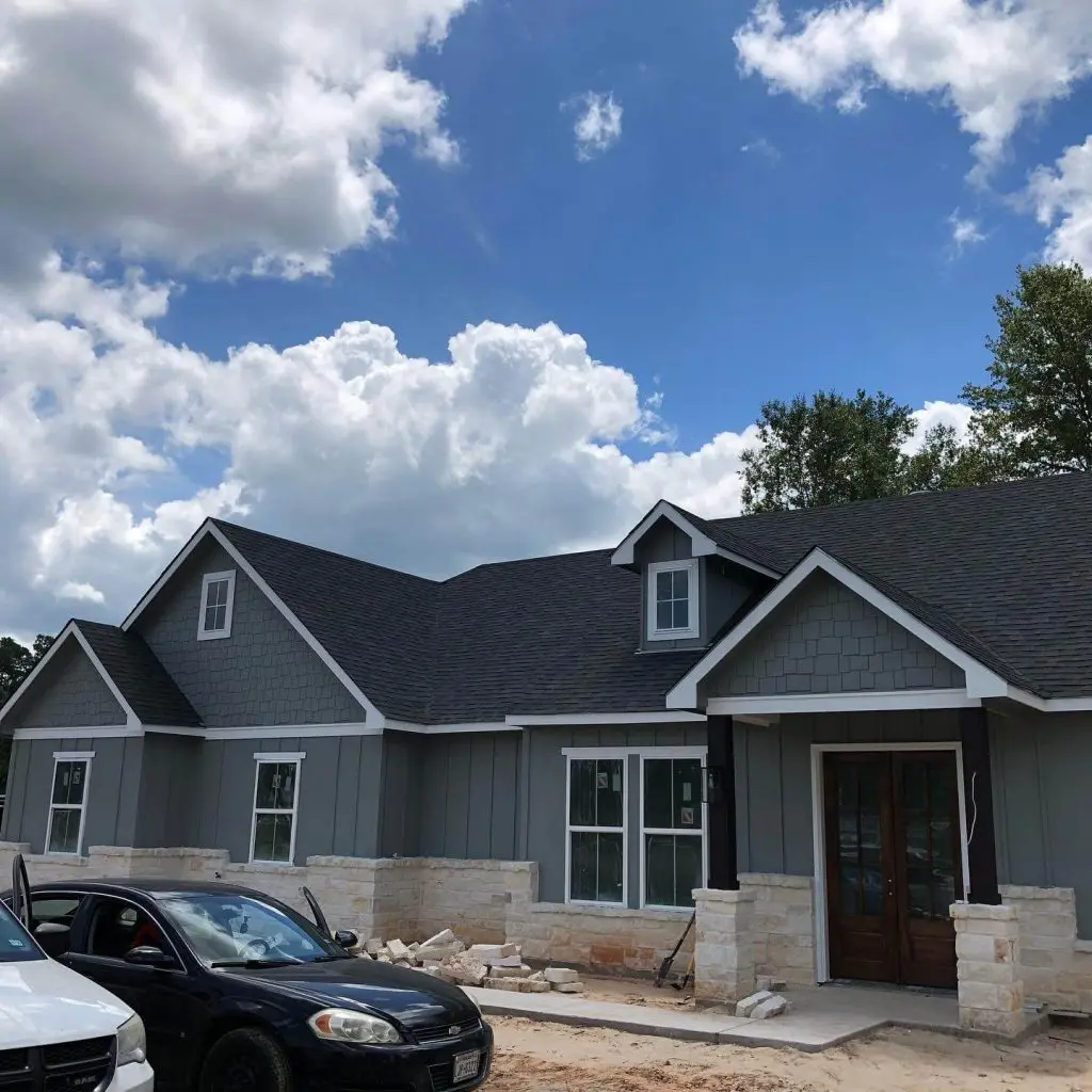 Painters in Lindale, TX specializing in exterior door refinishing, showcasing a custom matte black planked door and crisp white trim on a stone entryway for a luxury home.