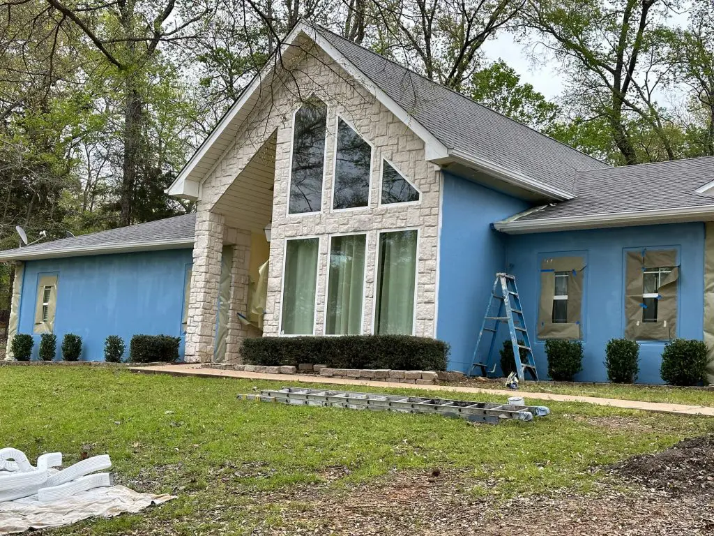 Expert exterior home painting for a luxury residence, showcasing a bold custom blue stucco color contrasted with white stone and trim in Tyler, TX.