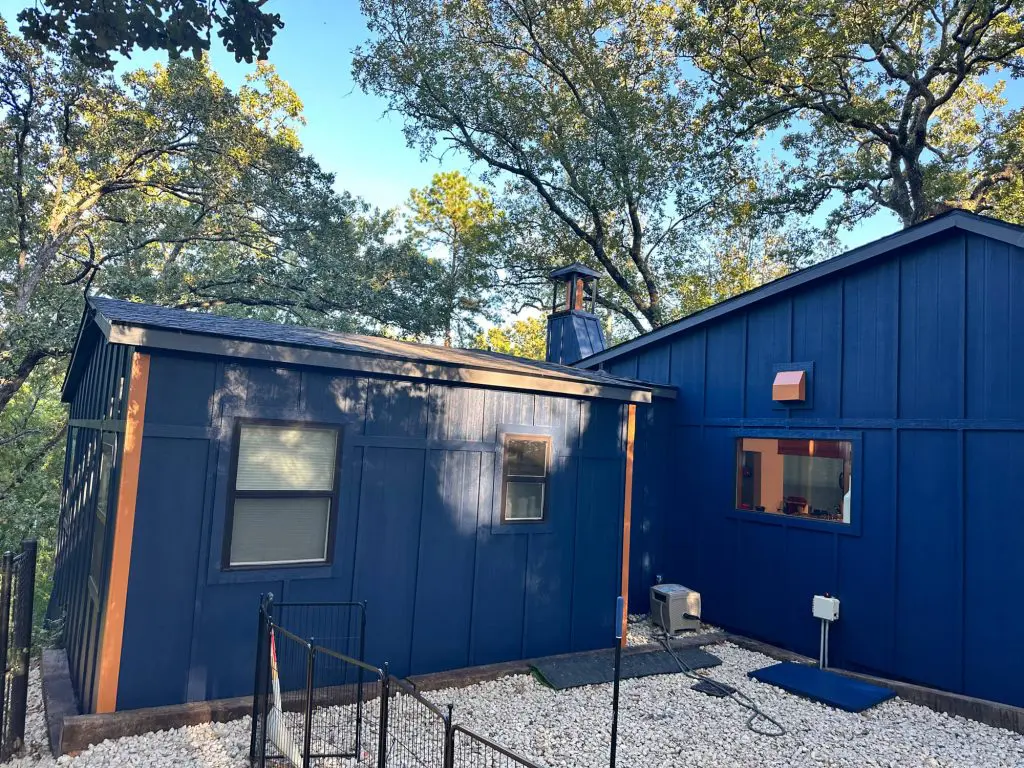 Painters in Tyler Tx providing high-quality exterior painting, transforming a wooded home with a custom, bold dark blue siding color and contrasting trim accents.