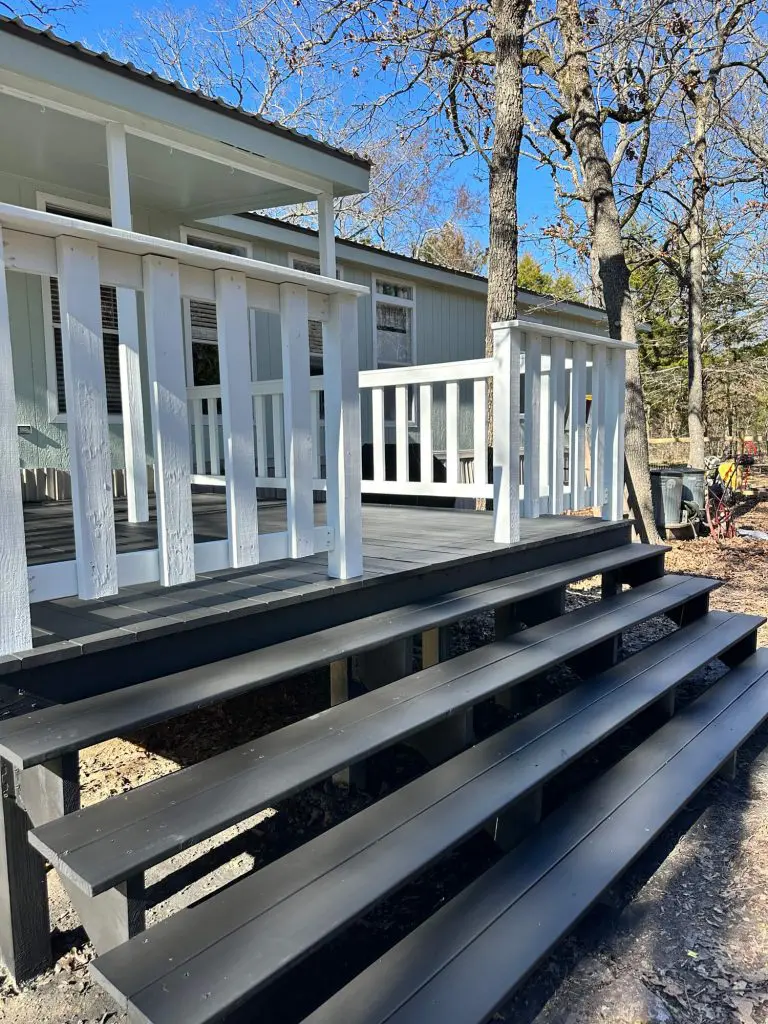Expert exterior deck painting and wood refinishing, showcasing contrasting white railings and dark gray steps on a wooded residential porch in the Tyler, TX area.