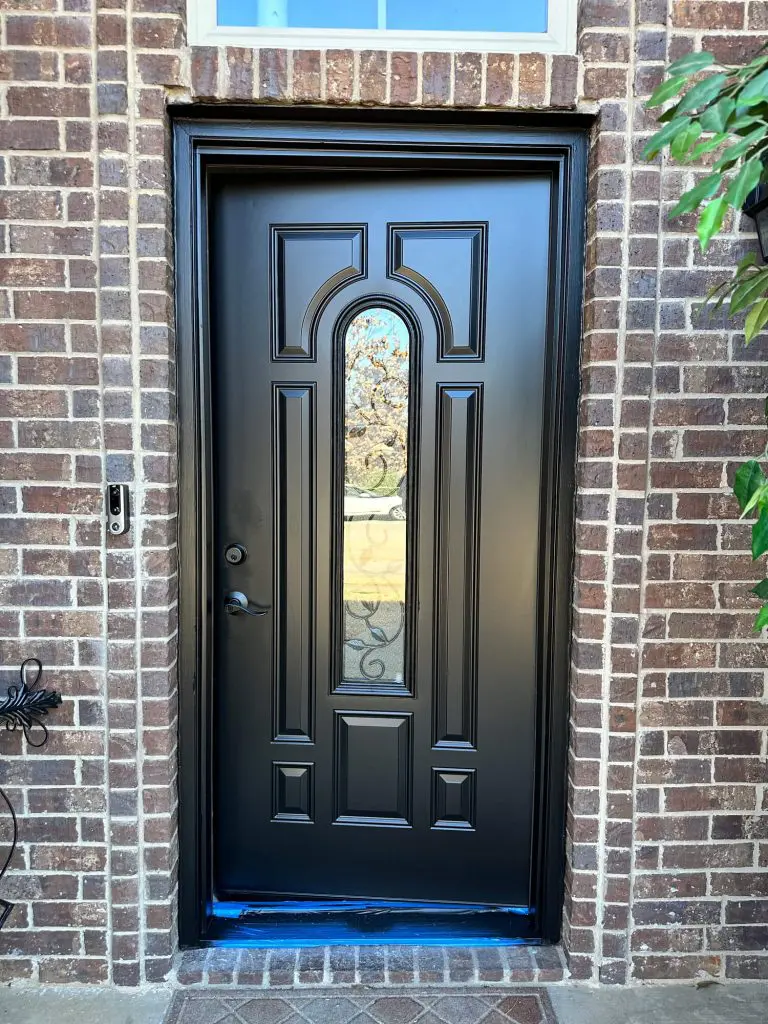 Expert exterior front door refinishing, showcasing a detailed panel door painted custom matte black with matching trim against a brick entryway in a Tyler, TX luxury home.