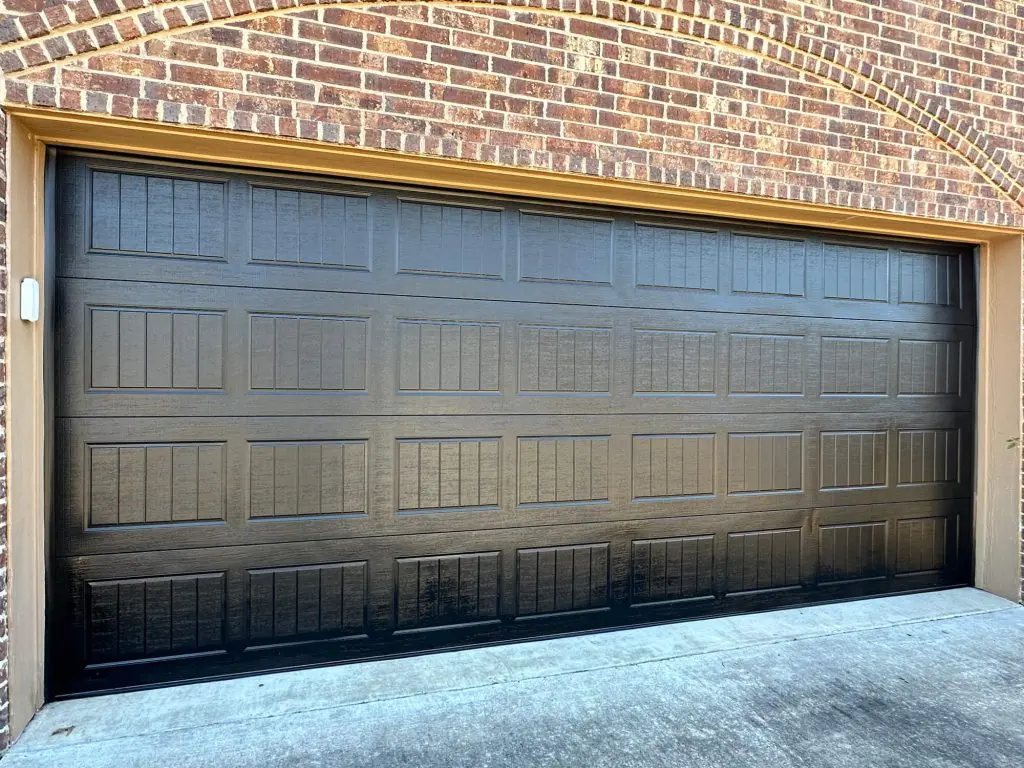 Expert exterior garage door painting showcasing a custom matte black finish against a traditional brick archway in a Tyler, TX residence.