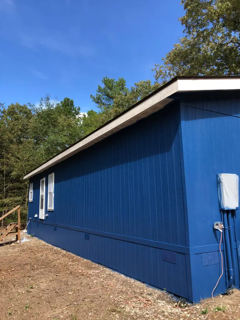 Expert exterior siding painting featuring a custom, bold royal blue color and contrasting white trim on a lakeside or residential property in the Tyler, TX area.