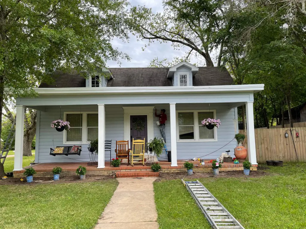 Exterior Painters Tyler, TX providing high-quality residential painting, shown actively finishing the custom light blue siding and crisp white trim of a charming front porch home.