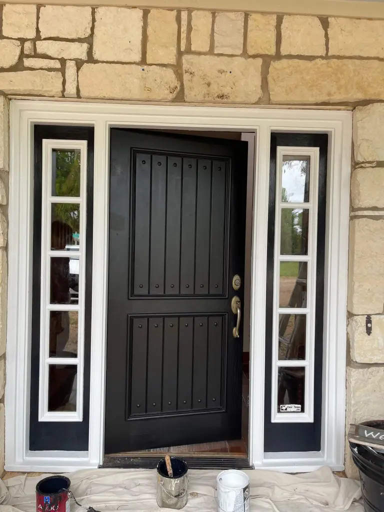 Expert exterior door painting and refinishing showcasing a custom matte black door with crisp white trim against a stone exterior in a Tyler, TX luxury home.