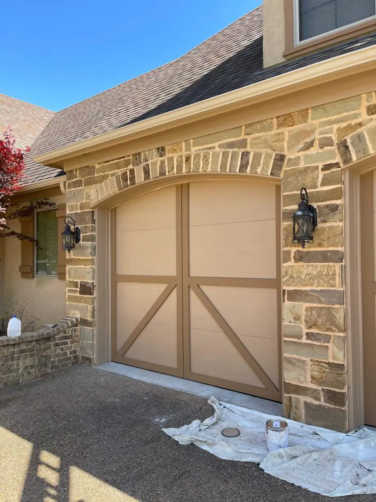 Expert exterior painting of a custom carriage house garage door in a cohesive tan color, enhancing the curb appeal of a stone and stucco luxury home in Tyler, TX.