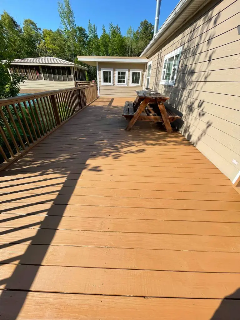 Professional deck staining and painting service on a large wooden deck and railing at a lakeside or wooded luxury home in the Tyler, TX area.
